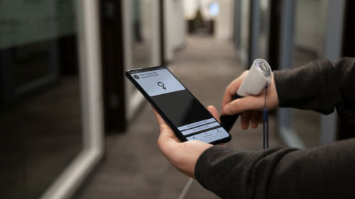 Two individuals walking in a building hallway using Hearsee’s first official cane prototype, engaged in conversation.