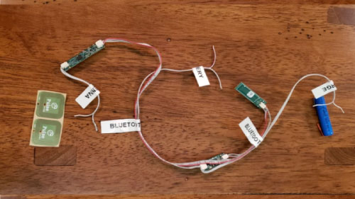 An overhead view of Hearsee's early prototype wiring layout on a wooden table, with labeled components including RFID tags, Bluetooth modules, and battery connections.